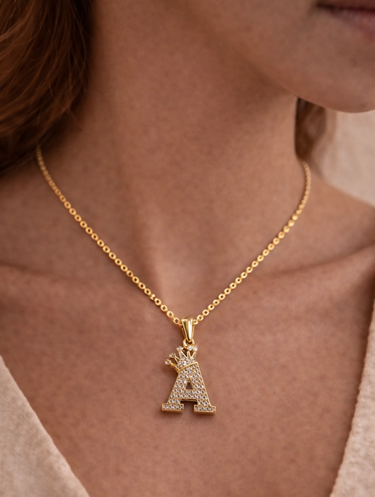 Gold necklace with a letter 'A' pendant on a person wearing a beige top.