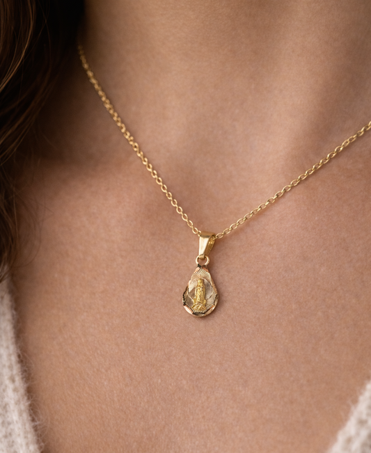 Gold necklace with a pendant on a person wearing a beige sweater.