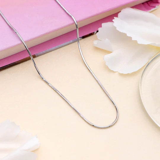 Silver necklace on a light pink surface with white flowers