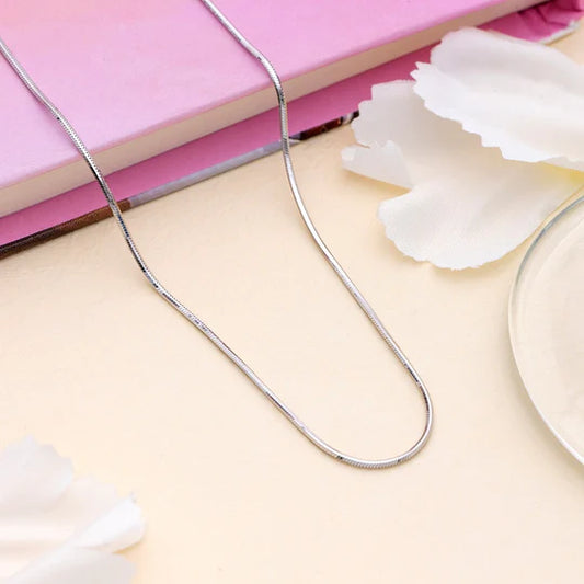 Silver necklace on a light pink surface with white flowers