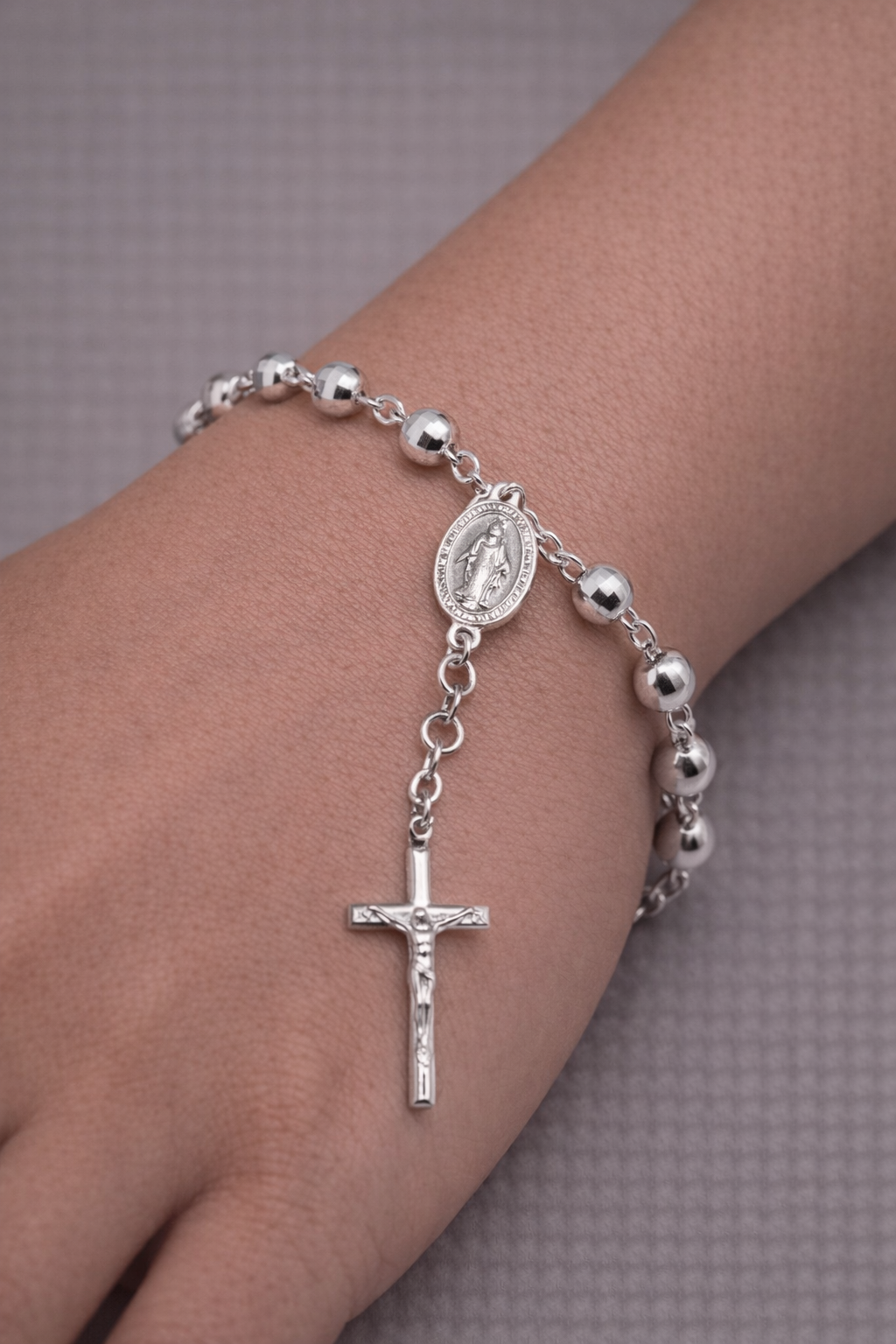 Silver rosary bracelet with a cross and medal on a wrist against a neutral background