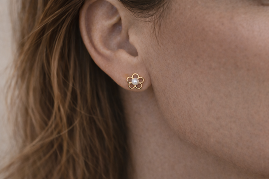 Close-up of an ear wearing a gold flower-shaped earring with a pearl center.