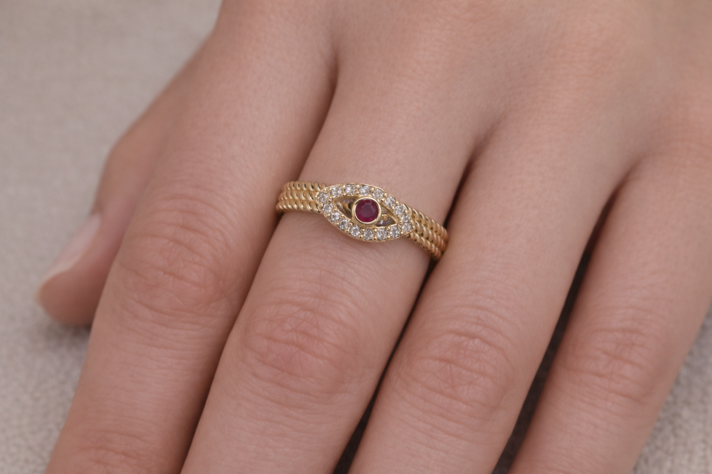 Gold ring with a red gemstone on a finger against a neutral background