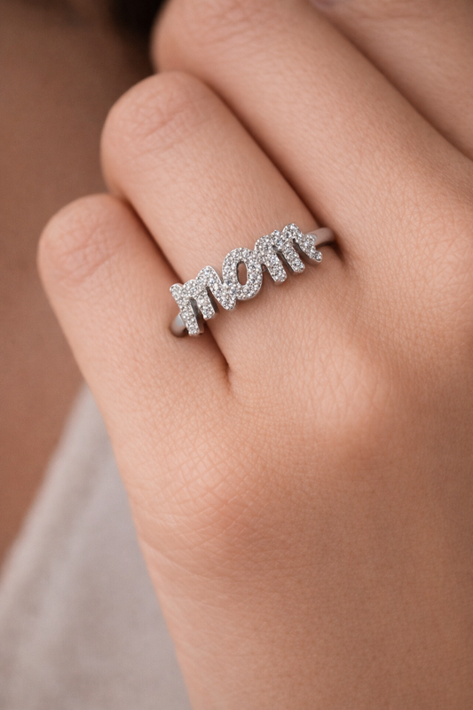 Silver 'MOM' ring on a person's finger with a blurred background