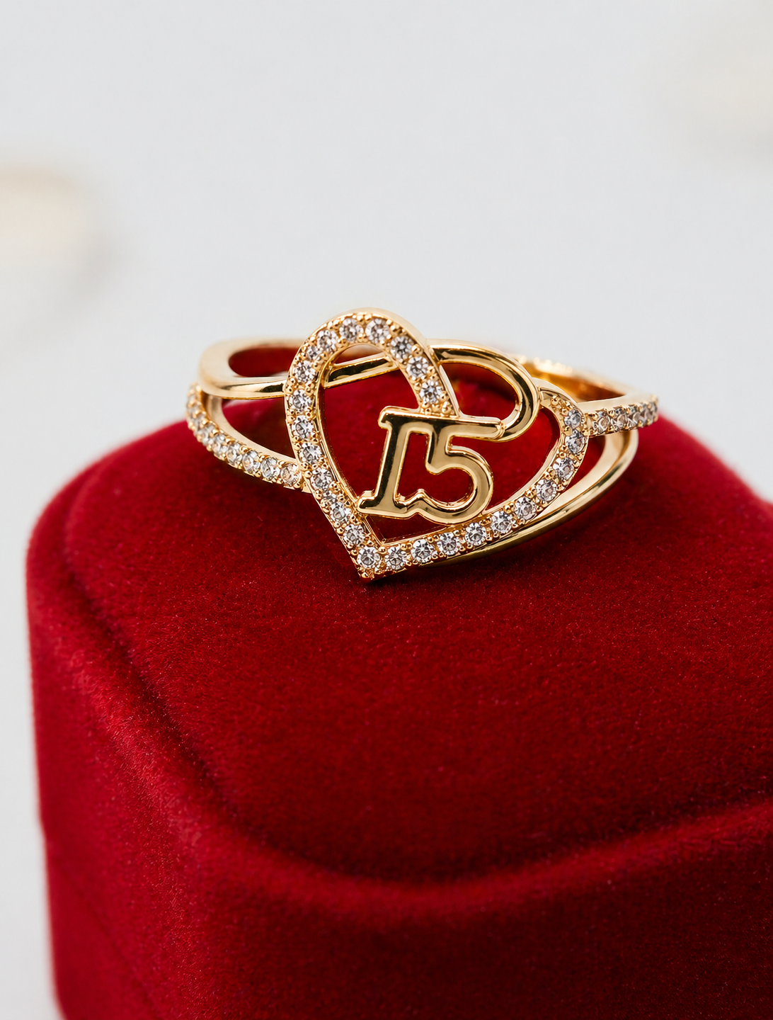 Gold heart-shaped ring with '15' design on a red cushion