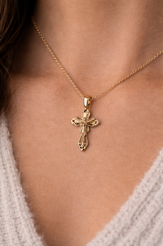 Gold necklace with a cross pendant on a person wearing a light-colored garment.