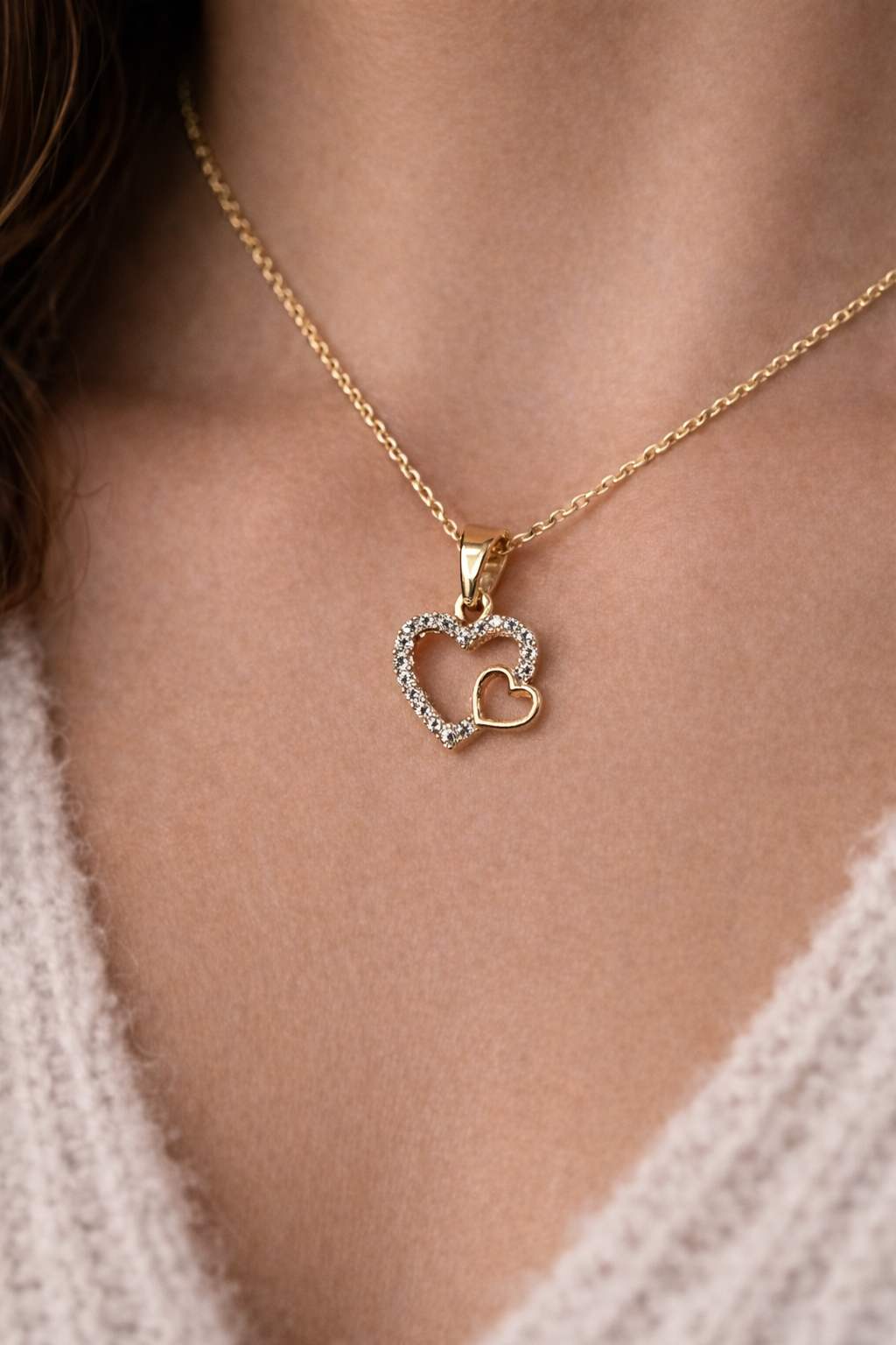 Gold necklace with a heart-shaped pendant on a person wearing a light-colored sweater.