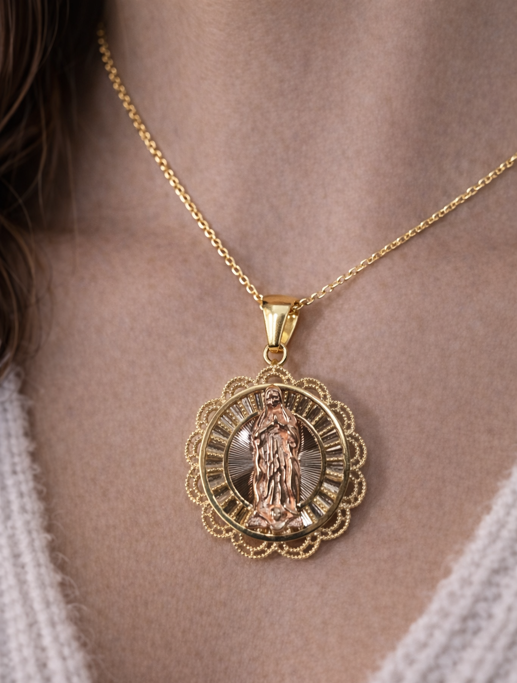 Gold necklace with a detailed pendant on a person wearing a white sweater.