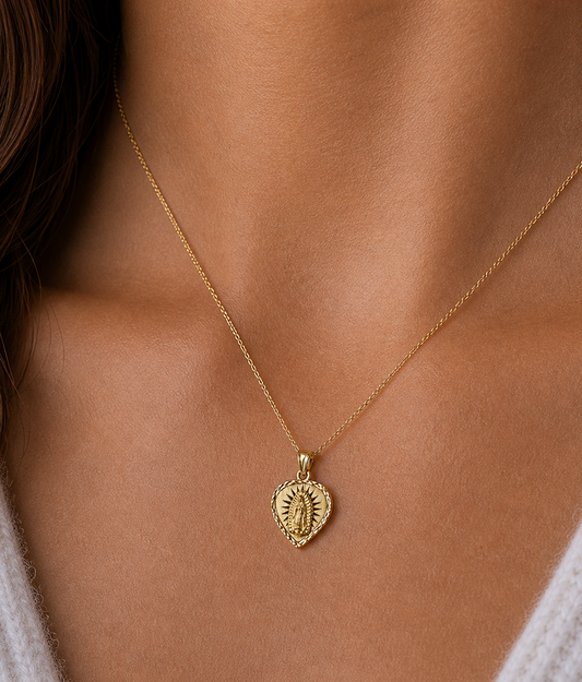 Gold necklace with a heart-shaped pendant on a person wearing a white sweater.