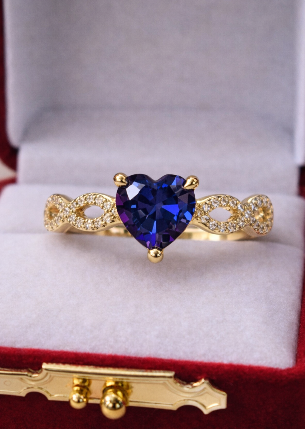Gold ring with a heart-shaped blue gemstone in a red jewelry box