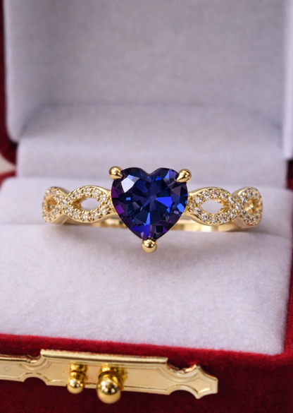 Gold ring with a heart-shaped blue gemstone in a red jewelry box