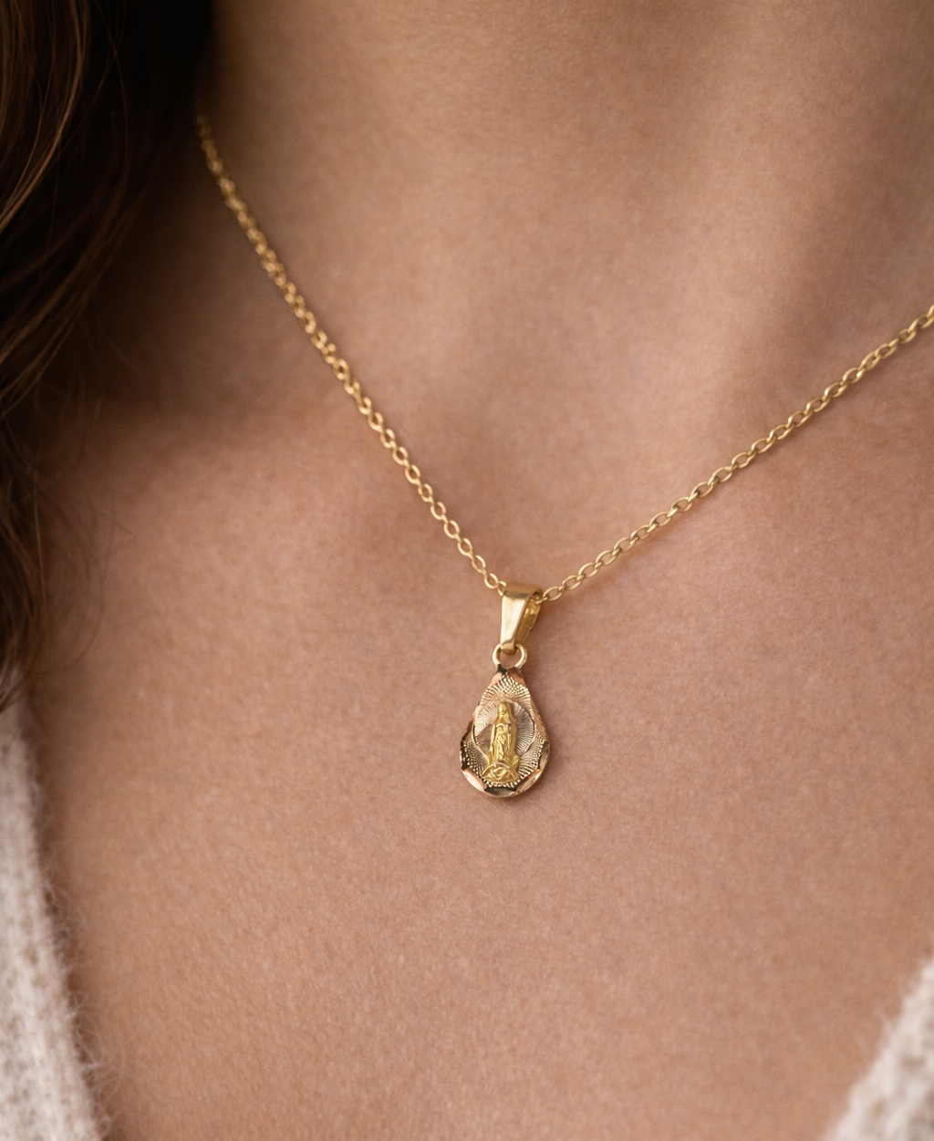 Gold necklace with a pendant on a person wearing a beige sweater.