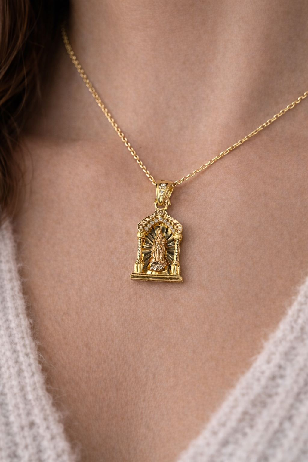 Gold necklace with a detailed pendant on a person wearing a light-colored sweater.
