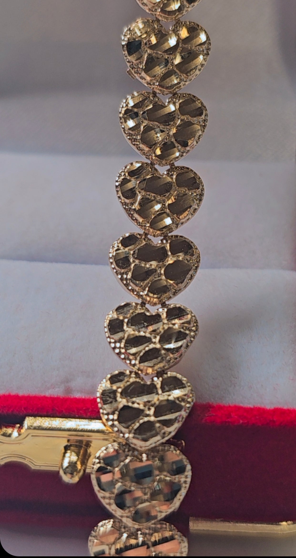 Gold bracelet with heart-shaped links on a red and white background